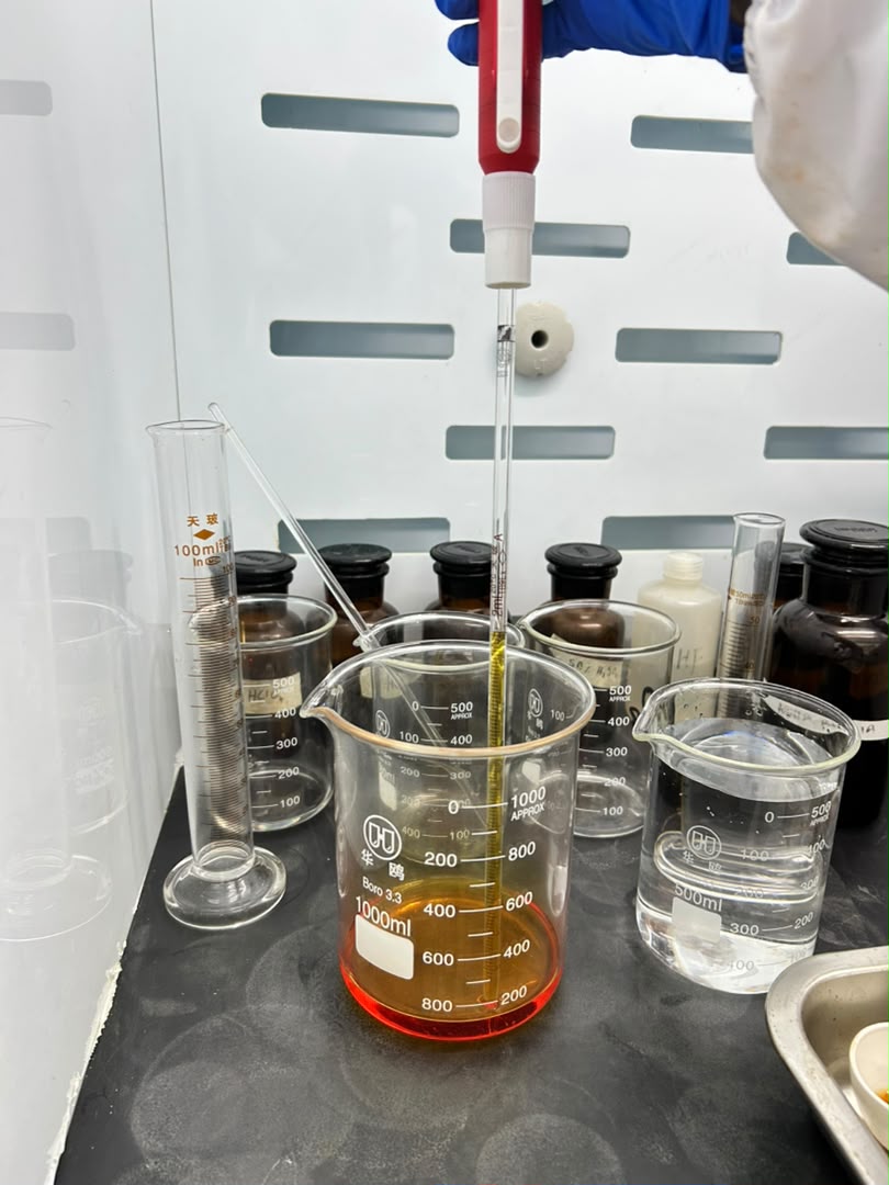 Laboratory analyst pipetting into a prepared sample solution inside a fume hood